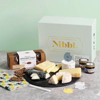 Nibbl Epic Board Gifting Box cheeseboard containing extra mature cheddar cheese, cantonnier cheese, Alexis de Portneuf brie and goat cheeses, cream brie, raincoast crisps crackers, cranberry and raspberry spread and fig, date and maple spread, with cheese picks, bee wax food wrap and a round slate charcuterie and cheeseboard