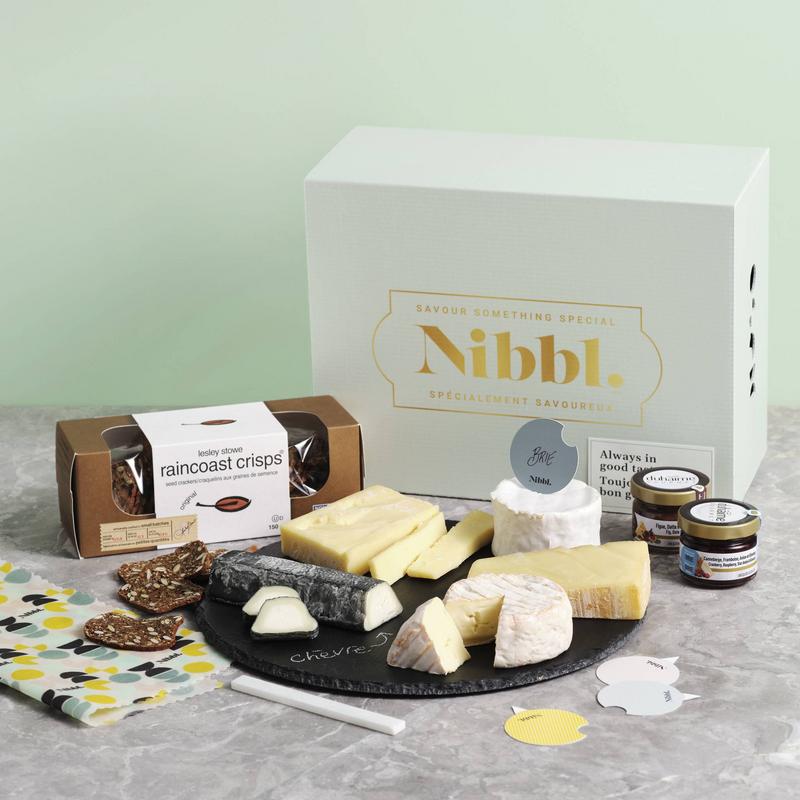 Nibbl Epic Board Gifting Box cheeseboard containing extra mature cheddar cheese, cantonnier cheese, Alexis de Portneuf brie and goat cheeses, cream brie, raincoast crisps crackers, cranberry and raspberry spread and fig, date and maple spread, with cheese picks, bee wax food wrap and a round slate charcuterie and cheeseboard